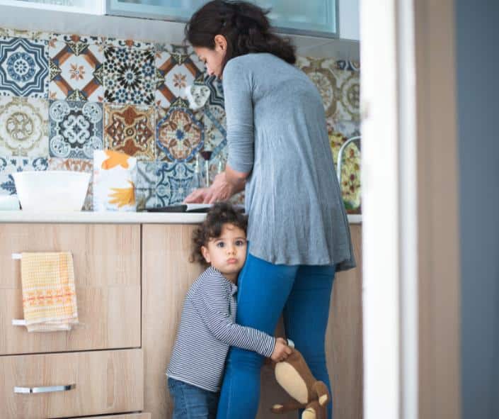 ילדה קטנה מחבקת את הרגל של אמא שלה בזמן שהיא במטבח